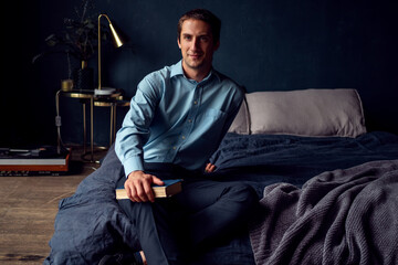 young man with a book is sitting on the bed, a portrait