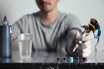 Tattoo artist with machine and ink at table, closeup