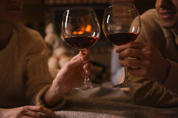 Couple with glasses of red wine near burning fireplace, closeup