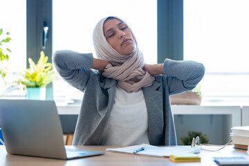 Tired young muslim business woman wearing hijab with neck pain at the office.