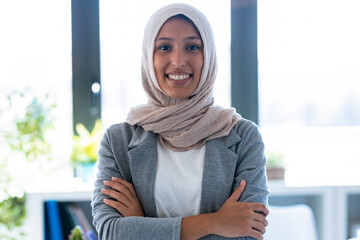 Smiling young muslim business woman wearing hijab looking at camera while standing up in the office.