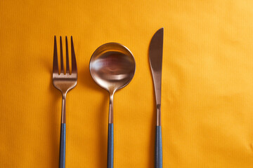 Stylish fork, spoon and knife on yellow background. Close-up.