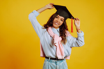 Portrait of Graduate woman in a graduation hat on her head.  Study, education, university, college, graduate concept on yellow banner.