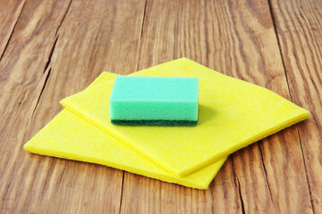 Household concept. Cleaning sponge and yellow micro fiber napkins on wooden background.