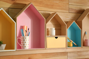 Painted house shaped shelves with different items on wooden wall. Interior elements