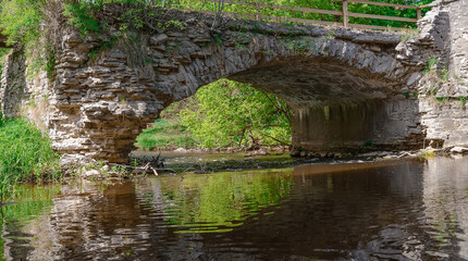 Fototapeta na wymiar Old stone bridge across small stream in the woods