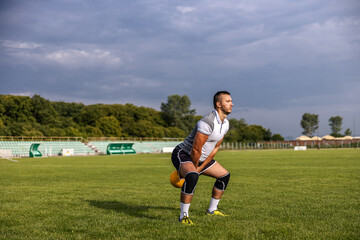 Attractive fit soccer player standing on the field and swinging kettle bell.