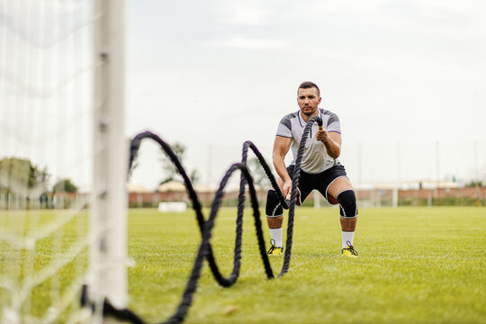 Soccer player doing exercises on the field. He is doing exercises with battle ropes.