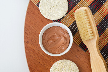 Red bentonite clay in the small white bowl, loofah sponge and massage body brush. Diy facial or hair mask, body wrap recipe. Natural beauty treatment and spa. Top view, copy space.
