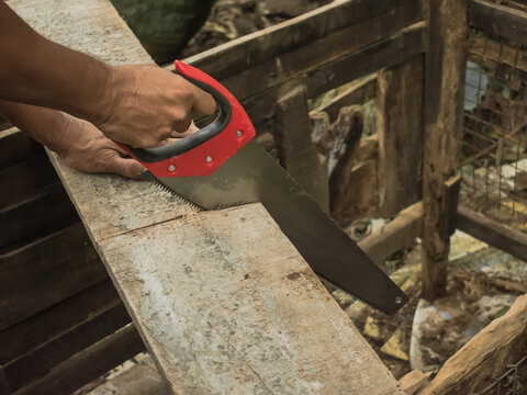 A man cutting a wooden board with the help of a hand saw, carpentry.