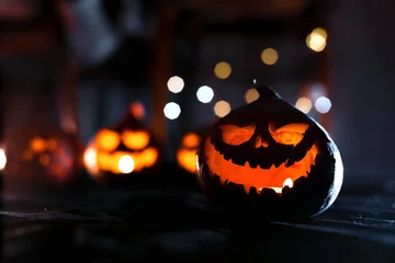 Foto op Plexiglas Halloween pumpkin jack o lantern with candles in the dark. Glowing eyes and mouth. Against the background of blurry jack-o'-lanterns and pumpkins with bokeh.  © Artem Rodionov