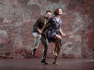 Foto op Canvas young couple dancing swing indoors in a studio against an old brick wall © karelian