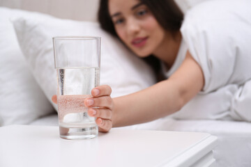 Young woman taking glass of water from nightstand at home, focus on hand