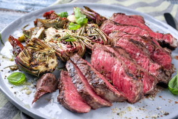 Traditional barbecue angus entrecote beef steak with artichoke hearts and herbs offered as close-up on a Modern Nordic design plate