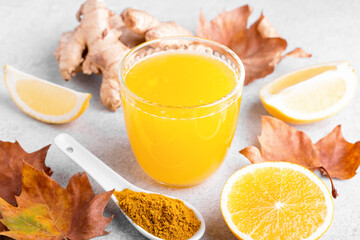 Immune boosting drink with citrus fruits, ginger, turmeric. Drink or smoothie with yellow fall leaves for autumn or virus season on neutral beige background