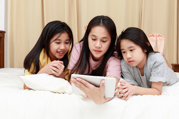 Happy Asian family enjoy and relax on bed in bedroom. mother and daughters enjoy using tablet together on bed.  Family concept.