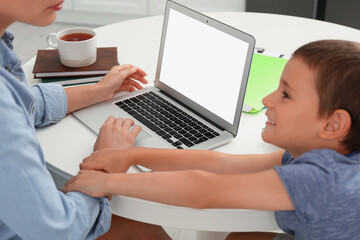 Little boy bothering mother with laptop at work in kitchen, closeup. Home office concept