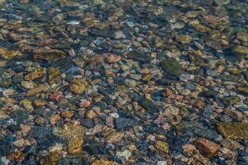 bright colored blue small pebbles in clear water sparkles in the sun, morning lake baikal