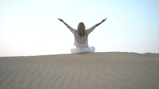 Woman holding scarf in the sand dune in desert meditating