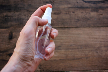 Female hand holding a sanitizer bottle on wooden background. Prevention of coronavirus concept