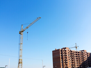 Fototapeta na wymiar Crane near the brick high-rise building under construction against the blue sky, modern construction