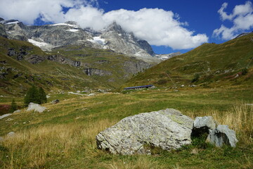 Fototapeta na wymiar Montagna e vallata in un paesaggio nella verde natura delle alpi con le vette innevate con una nuvola sulla cima