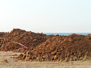 A pile of clay and a red danger warning tape. Dig a ditch in clay soil and fill with water.