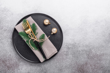 Christmas table setting with black ceramic plate, gifts and fir tree branch on stone background. Top view. Copy space