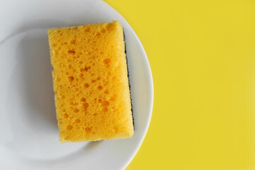 yellow dish washing sponge on a white plate on a yellow background. flat lay. copy space. housework concept.

