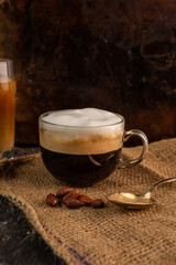 a glass of aromatic, fresh coffee with white, milk foam, on a rustic, warm background