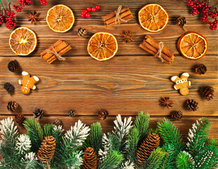 Christmas or New Year background. Fir branches, red berries, fir cones, dried orange slices, spices and gingerbread men on the wooden background. Top view. Text space.