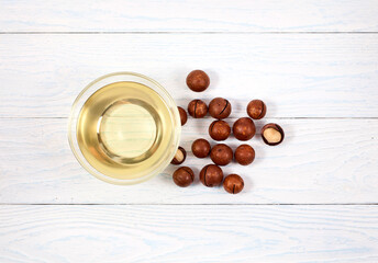 Macadamia nuts and macadamia oil in a glass bowl on a white wooden background. Top view.