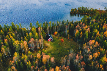 Aerial view of log cabin in autumn colors forest by blue lake in rural fall
