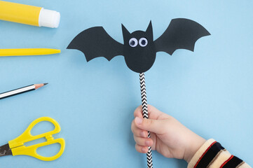 Halloween handmade decor. Child makes funny paper bat. Glue toy eyes. Step 5. Top view, flat lay