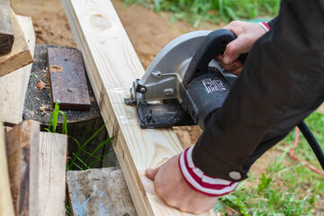 Sawing a wooden Board with an electric grinder. A man saws wooden planks using a fast-rotating metal saw blade.