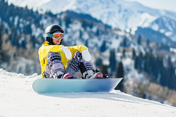 Fototapeta na wymiar Young woman snowboarder sitting in the snow and exploring the slope before the descent