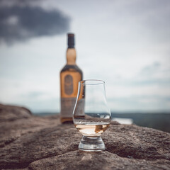 Glencairn glass with a dram of scotch whisky with a blurred scotch bottle in the background.