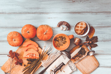 Pumpkin soup on blue wooden table, linen cloth, vintage cutlery. Autumn cream soup, seeds and parsley. Sliced herbs, pumpkin on cutting board, cooking process. Thanksgiving dinner, flat lay, top view.