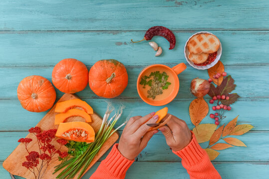 Pumpkin soup on blue wooden table with linen cloth and vintage cutlery. Woman hands cutting vegetables, cooking process. Autumn vegetarian, healthy food concept. Thanksgiving dinner, top view.