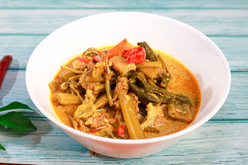 Thai food is called Kaeng The Po. Morning glory pork belly in a white cup on a blue wooden floor. View from close range.