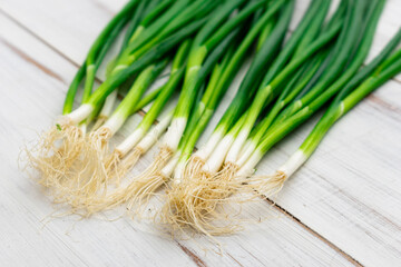 A bunch of green onions on a light wooden background.