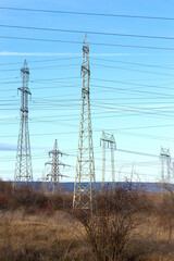 High voltage lines and power pylons in a flat and green agricultural landscape on a sunny day with cirrus clouds in the blue sky. Pylon and transmission power line