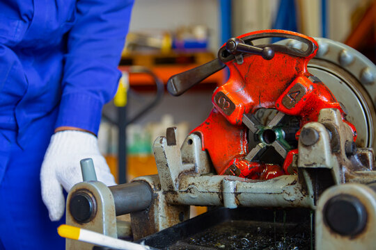 The worker threading the pipe with a Pipe Threading Machine in the workshop. Selective Focus.