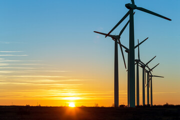 Obraz premium Wind Turbines at Dusk. Landscape sunset with windmills. Renewal source of electricity. Wind turbines field new technology for clean energy on mountain, sunset view with colorful twilight on sky