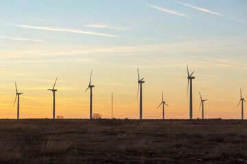 Obraz premium Wind Turbines at Dusk. Landscape sunset with windmills. Renewal source of electricity. Wind turbines field new technology for clean energy on mountain, sunset view with colorful twilight on sky