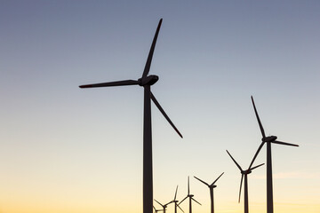 Fototapeta premium Wind Turbines at Dusk. Landscape sunset with windmills. Renewal source of electricity. Wind turbines field new technology for clean energy on mountain, sunset view with colorful twilight on sky