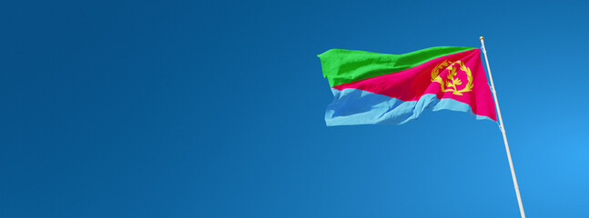 The beautiful flag of Eritrea waving against a blue sky in wide format. Eritrea national flag on background