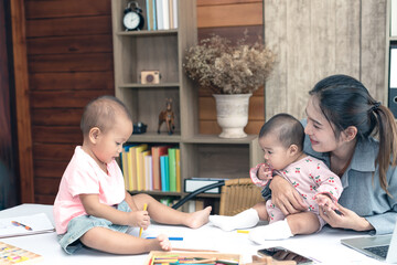 Busy woman trying to work while babysitting two daughter.  Young beautiful Asian mother holding little baby on lap while another daughter playing around her. Working women with multitasking.