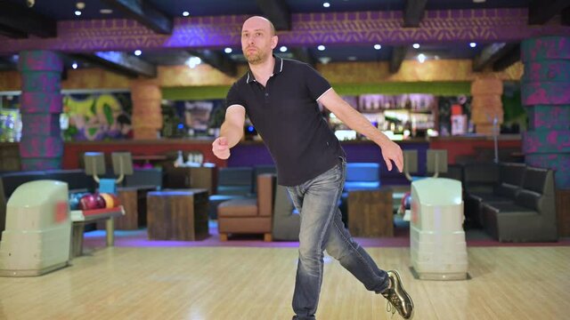 Bald man throws a ball while bowling
