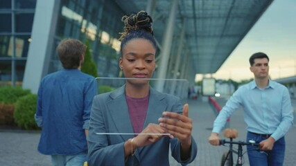 Attractive black business woman using digital tablet for communications browsing holographic transparent screen application for animation outdoors. Airport. - Powered by Adobe